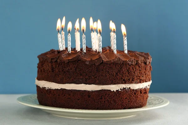 Delicioso pastel de chocolate con velas en la mesa sobre fondo azul —  Fotos de Stock