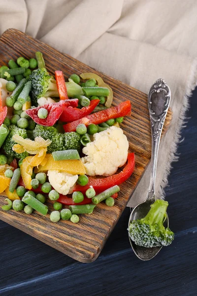 Verduras congeladas sobre tabla de cortar, sobre servilleta, sobre fondo de mesa de madera — Foto de Stock