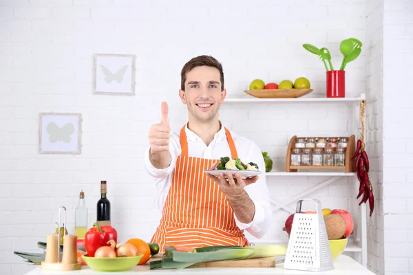 Hombre en la mesa con diferentes productos y utensilios en la cocina sobre fondo de pared blanco —  Fotos de Stock