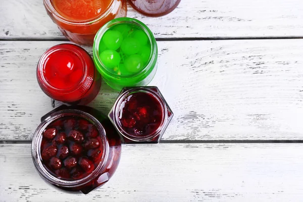 Homemade jars of fruits jam on color wooden planks background