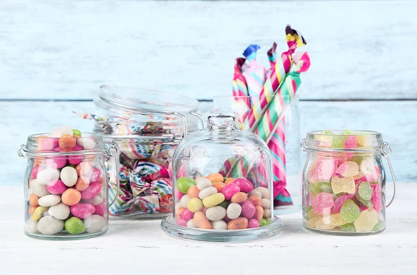 Багатобарвні цукерки в скляних банках на кольоровому дерев'яному фоні — стокове фото