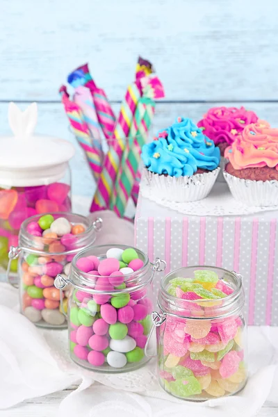 Multicolor candies in glass jars and cupcakes on color wooden background — Stock Photo, Image