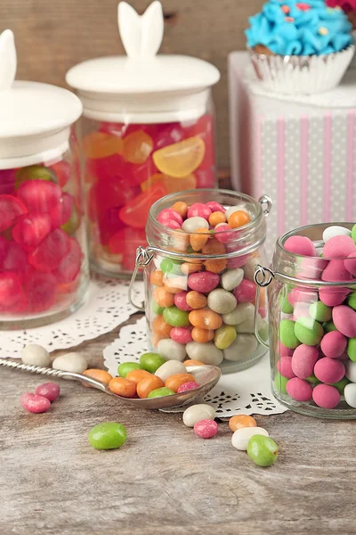 Bonbons multicolores dans des pots en verre et des cupcakes sur fond en bois — Photo