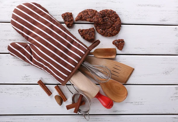 Set of kitchen utensils with cookies in mitten on wooden background — Stock Photo, Image