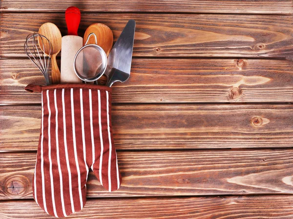 Set of kitchen utensils in mitten on wooden planks background — Stock Photo, Image