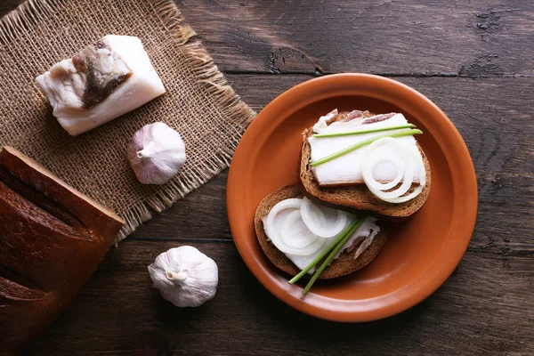 Sandwiches with lard on plate and garlic on wooden background — Stock Photo, Image