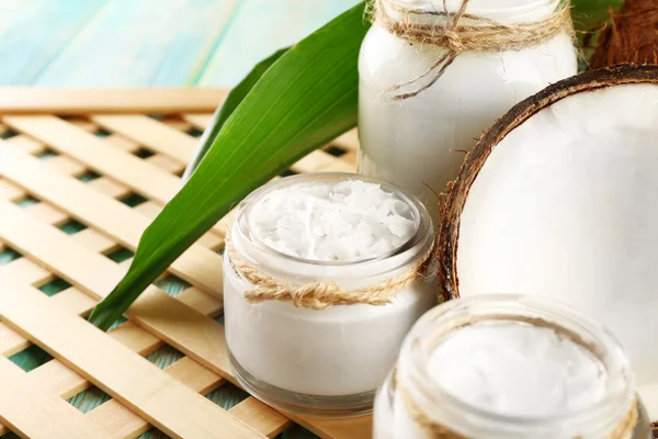 Aceite de coco fresco en cristalería sobre tabla de madera de color y fondo de bandeja de rejilla — Foto de Stock