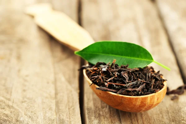 Svart te med blad i sked på gamla träbord — Stockfoto
