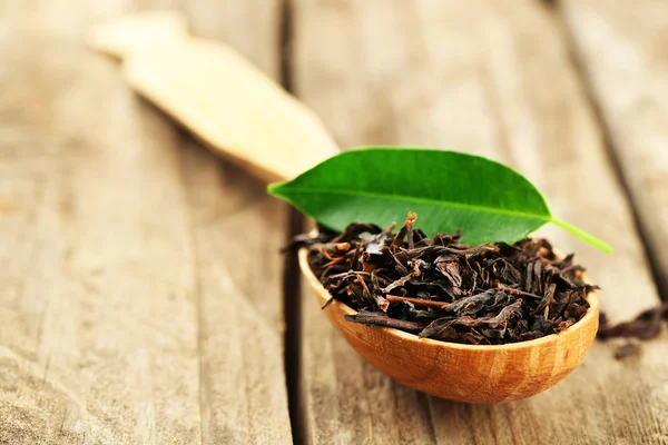 Black tea with leaf in spoon on old wooden table — Stock Photo, Image