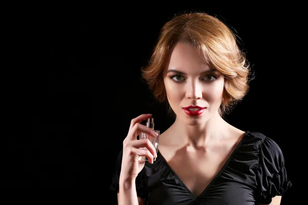 Bella giovane donna con bottiglia di profumo su sfondo nero — Foto Stock