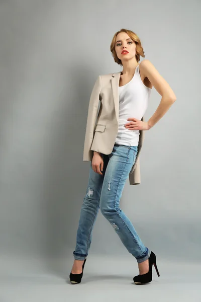 Hermosa joven con chaqueta y jeans posando sobre fondo claro — Foto de Stock