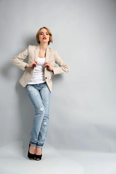 Красива молода жінка в куртці і джинсах позує на світлому фоні — стокове фото