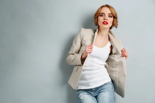 Mooie jonge vrouw in jas en jeans poseren op lichte achtergrond — Stockfoto