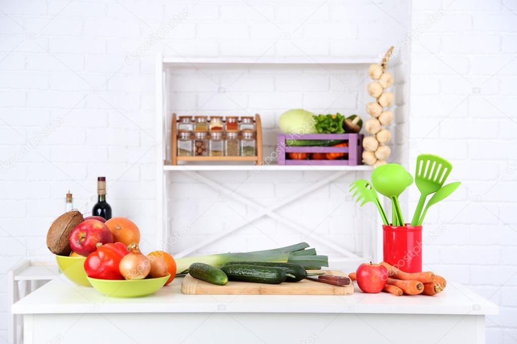 Table with different products in kitchen on white wall background