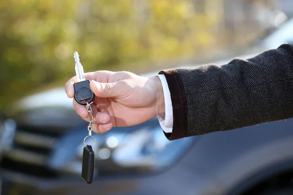 Male hand with car key on car background