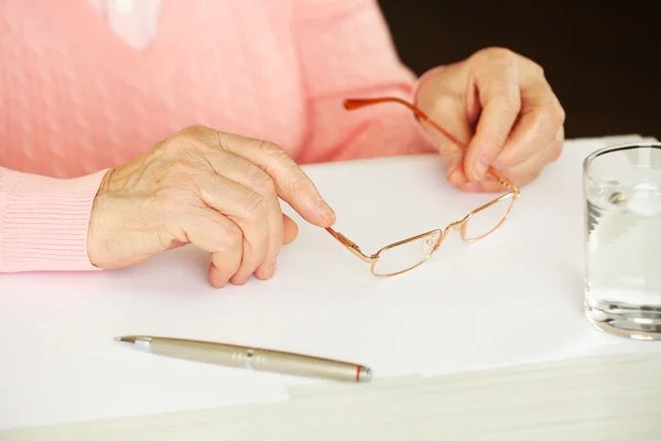 Manos de mujer adulta con bolígrafo, vasos y vaso de agua sobre la mesa, sobre fondo oscuro — Foto de Stock