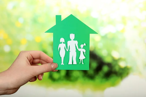 Cutout hus med papper familj i kvinnlig hand på ljusa suddig bakgrund — Stockfoto