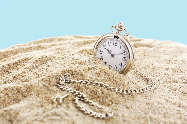 Silver pocket clock on sand on blue background — Stock Photo, Image