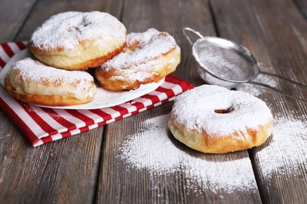 Delicious donuts with icing and powdered sugar on wooden background