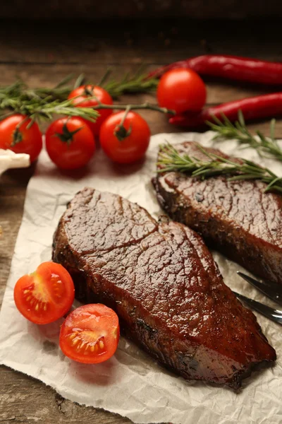 Composição com saborosa carne assada em folha de papel, tomates e raminhos de alecrim em fundo de madeira — Fotografia de Stock