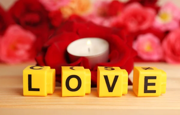 Letras decorativas formando palavra AMOR com flores e vela sobre fundo brilhante — Fotografia de Stock