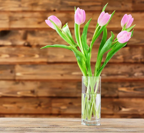 Lindas tulipas cor-de-rosa em vaso na mesa sobre fundo de madeira — Fotografia de Stock