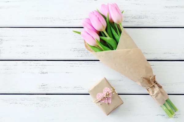 Красивые розовые тюльпаны в бумаге с настоящей коробкой на деревянном фоне — стоковое фото