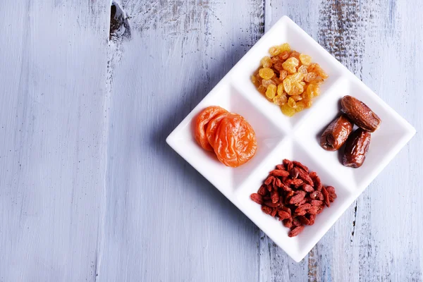 Getrocknete Früchte in weißem Teller auf farbigem Holztischhintergrund — Stockfoto