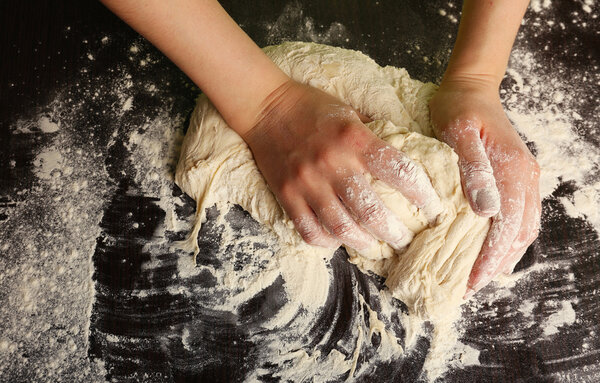Making dough by female hands on wooden table background