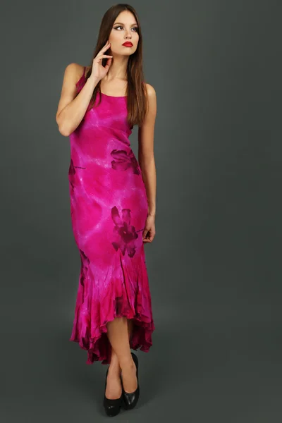 Красива молода жінка в довгій рожевій сукні на темно-сірому фоні — стокове фото