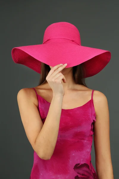 Beautiful young woman in pink dress and hat on dark gray background — Stock Photo, Image