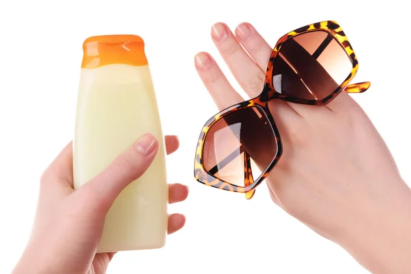 Bottle of suntan cream and sunglasses in female hands isolated on white — Stock Photo, Image