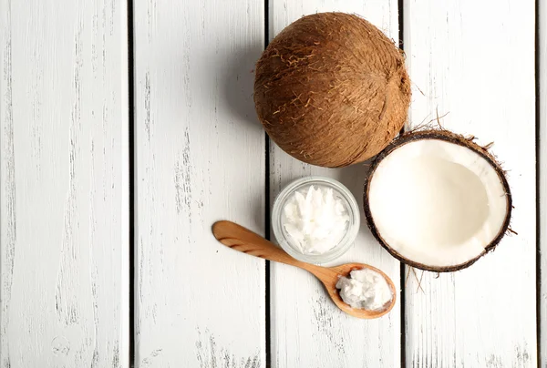 Coconut with coconut oil in jar on wooden background