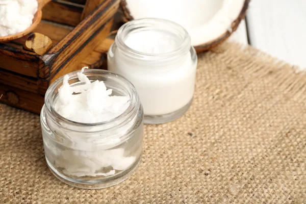 Kokos met potten van kokosolie en cosmetische crème op zak achtergrond — Stockfoto