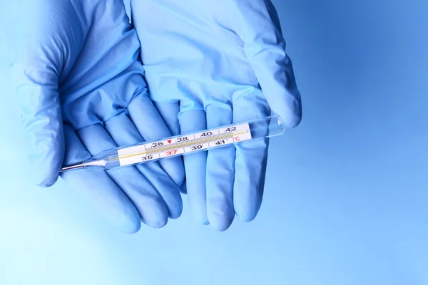 Hände mit Handschuhen halten Thermometer auf blauem Hintergrund — Stockfoto