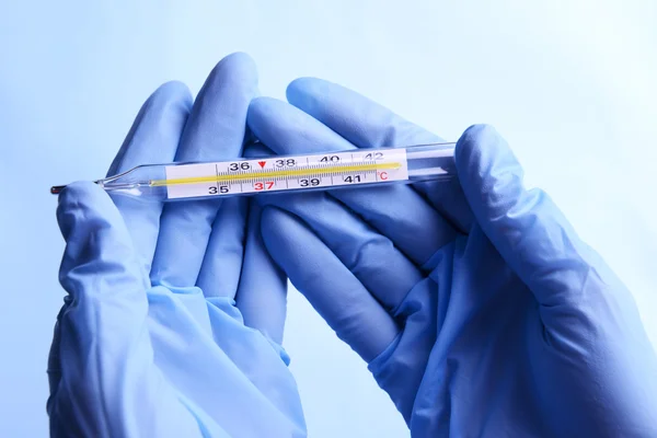 Hands with gloves holding thermometer on blue background — Stock Photo, Image