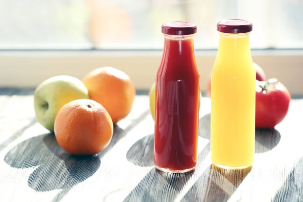 Bottles of juice with fruits and vegetables on windowsill — Stock Photo, Image