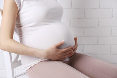 Açık renkli sandalye üzerinde oturan genç hamile kadın