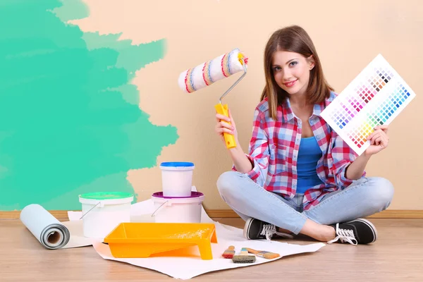 Hermosa chica sentada en el suelo con el equipo para pintar la pared —  Fotos de Stock