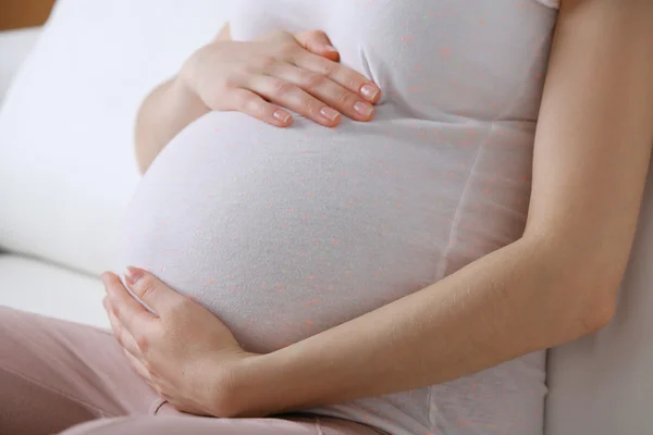 Unga gravid kvinna sitter på soffan på nära håll — Stockfoto