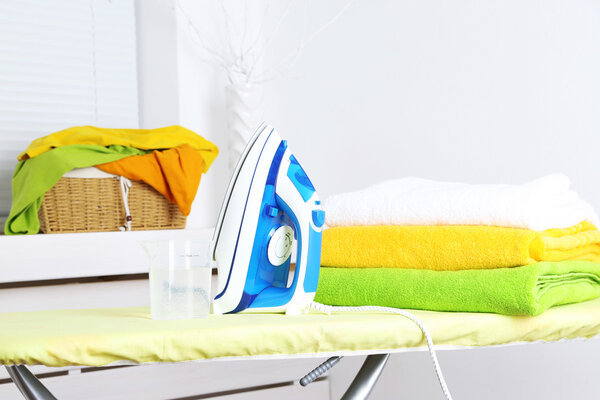 Iron with towels on ironing board on light home interior background