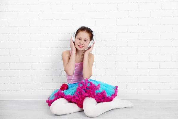 Bela pequena bailarina com fones de ouvido em tijolos brancos fundo da parede — Fotografia de Stock