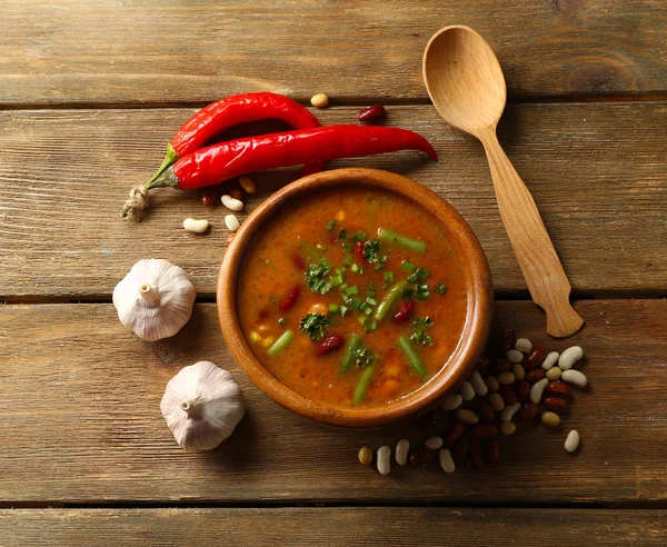 Фасолевый суп в миске и ингредиенты на фоне деревянного стола — стоковое фото
