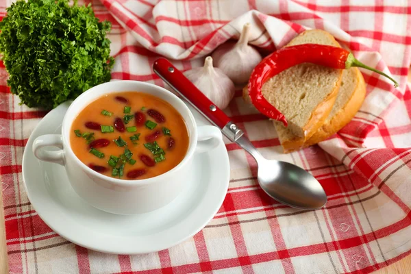 Фасолевый суп в миске со свежим нарезанным хлебом на салфетке, на фоне деревянного стола — стоковое фото