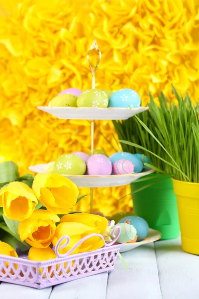 Huevos de Pascua sobre jarrón y tulipanes sobre mesa sobre fondo amarillo — Foto de Stock