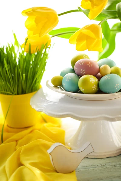 Huevos de Pascua en jarrón y tulipanes en mesa sobre fondo brillante — Foto de Stock