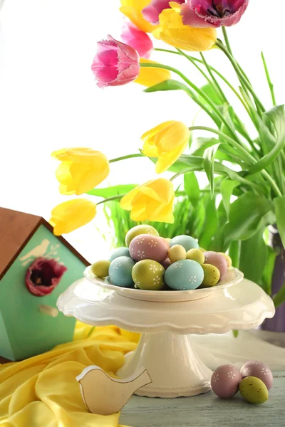 Velikonoční vejce na vázu a tulipány na stole na světlé pozadí — Stock fotografie