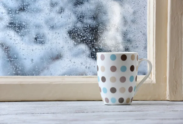 Cup of hot drink on windowsill on rain background — Stock Photo, Image