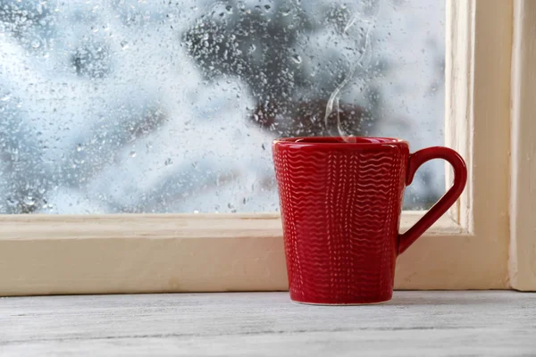 Copa de bebida caliente en el alféizar de la ventana sobre fondo de lluvia —  Fotos de Stock