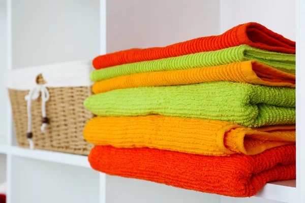 Colorful towels with wicker basket on shelf of rack background — Stock Photo, Image